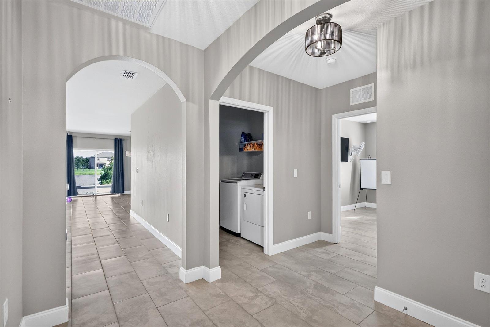 A hallway with arched openings leads to a laundry closet and a room with tile flooring — 8649 Cobblestone Drive, Fort Pierce FL 34945, FORT PIERCE, FL