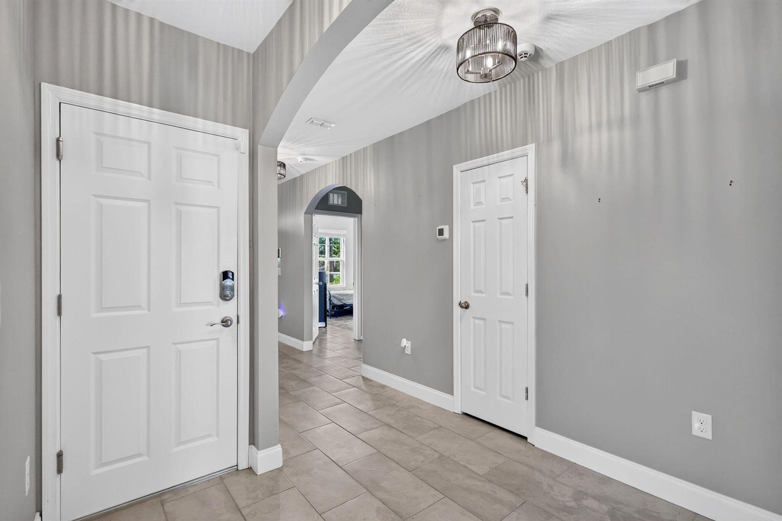 A gray-walled entryway features a white door, tiled flooring, and an arched hallway passage — 8649 Cobblestone Drive, Fort Pierce FL 34945, FORT PIERCE, FL