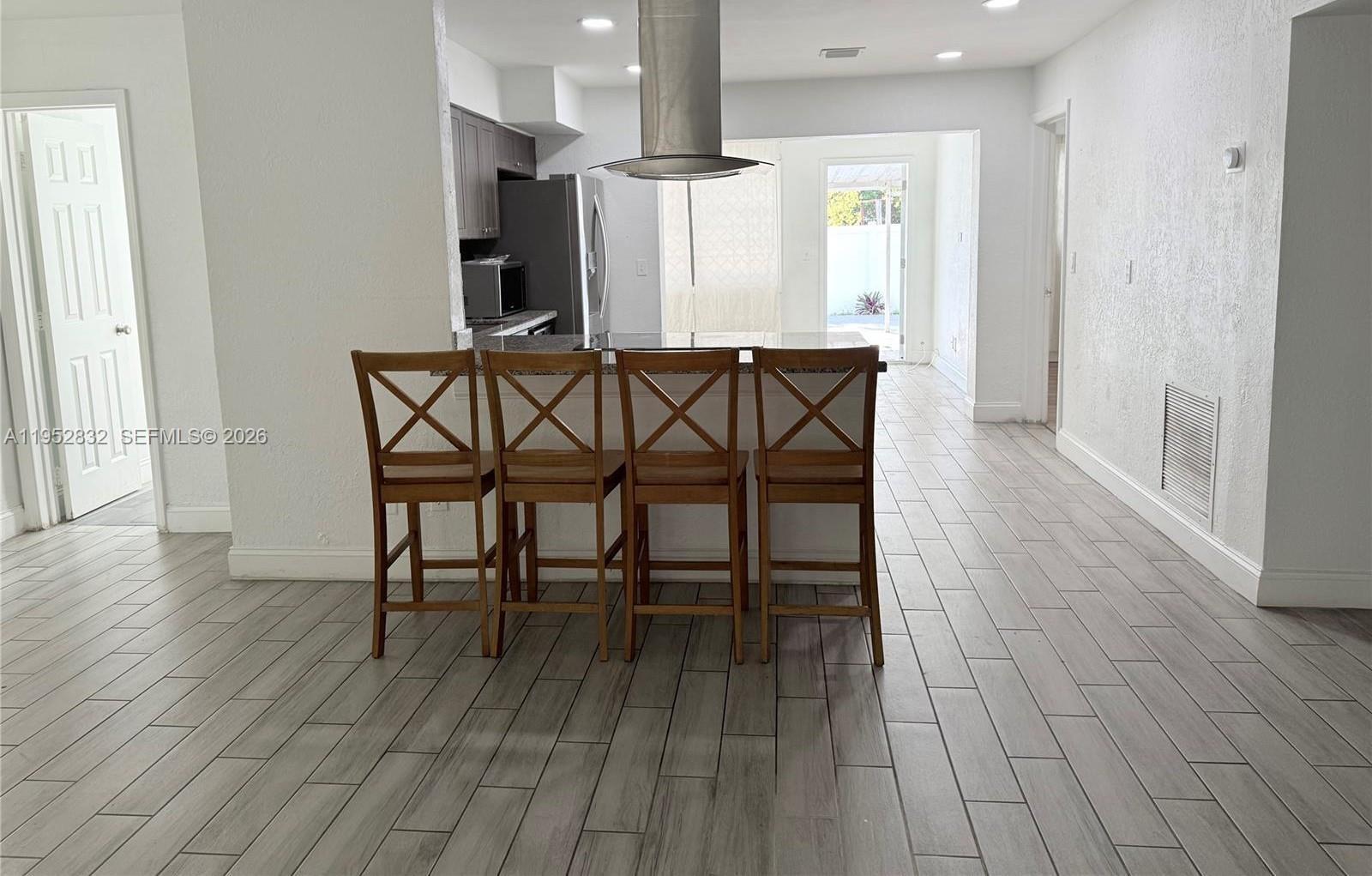 A kitchen island with four wooden chairs sits on a light-colored tiled floor — 4741 SW 25th Terrace, Dania Beach FL 33312, DANIA BEACH, FL