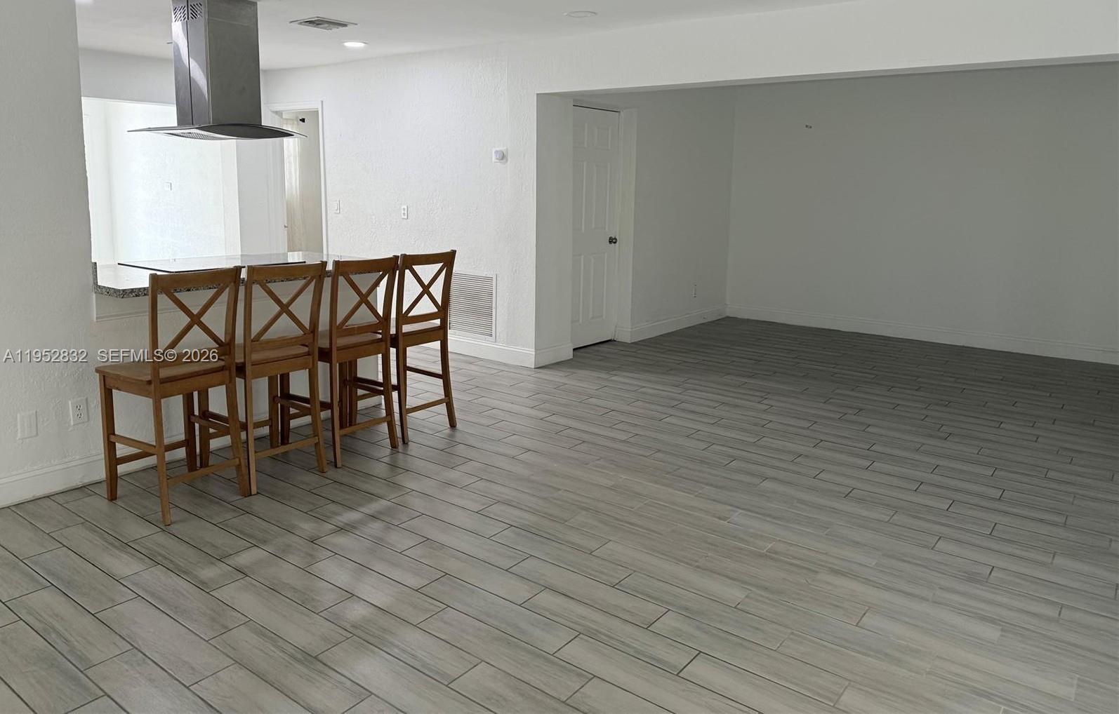 A kitchen island with four wooden chairs sits in a room with gray tile flooring — 4741 SW 25th Terrace, Dania Beach FL 33312, DANIA BEACH, FL