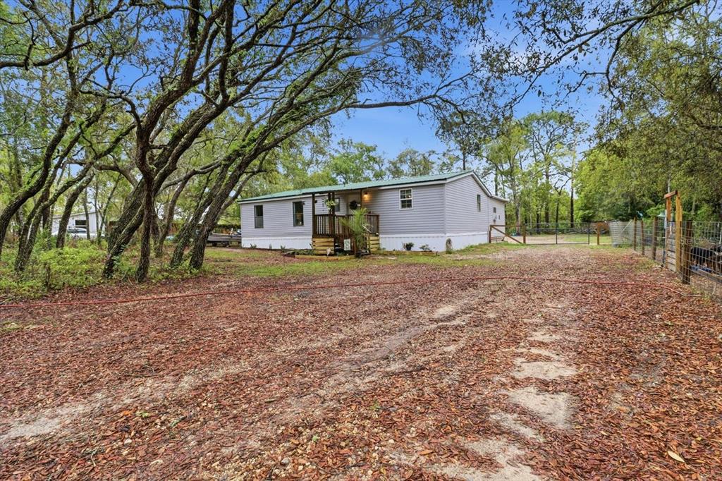 A single-story manufactured home with grey siding sits on a wooded lot with a dirt driveway — 5114 W ROCHELLE STREET, HOMOSASSA, FL