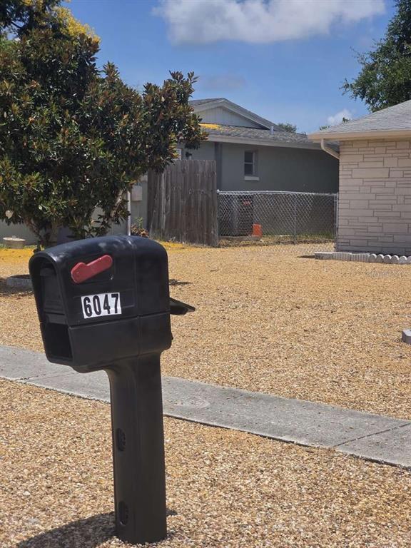 A black mailbox with the number 6047 stands in a gravel yard before a house — 6047 9TH AVENUE, NEW PORT RICHEY, FL