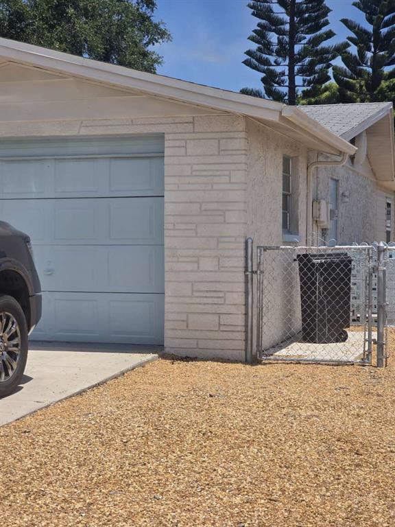 A light-colored brick garage exterior with a gravel driveway and a chain-link fenced area — 6047 9TH AVENUE, NEW PORT RICHEY, FL