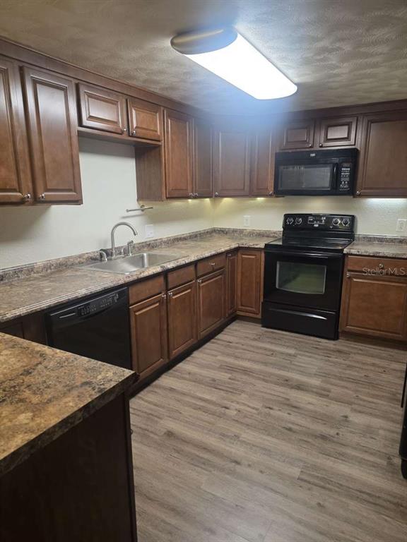 A kitchen featuring wood cabinets, dark countertops, black appliances, and light-colored wood-look flooring — 6047 9TH AVENUE, NEW PORT RICHEY, FL