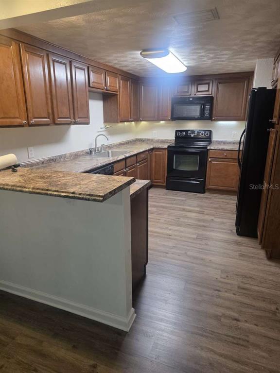 A kitchen features wood cabinets, laminate countertops, black appliances, and light-colored wood-look flooring — 6047 9TH AVENUE, NEW PORT RICHEY, FL