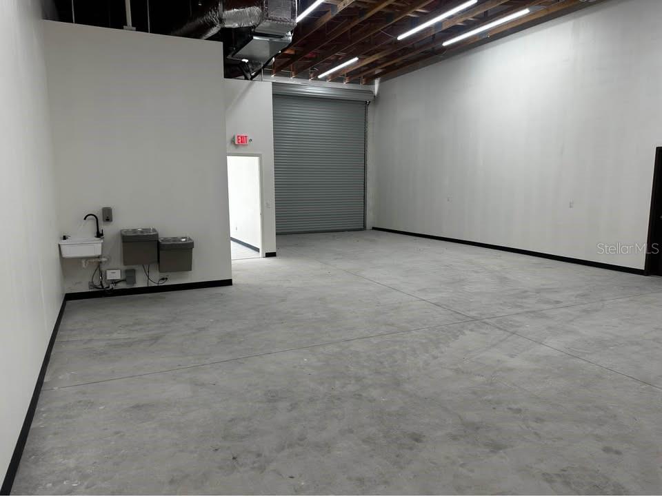 An industrial warehouse space features a concrete floor, a roll-up door, and a utility sink — 18803 TITUS, HUDSON, FL
