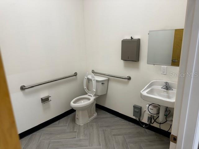 A small, accessible restroom features a toilet, a wall-mounted sink, and gray herringbone flooring — 18803 TITUS, HUDSON, FL