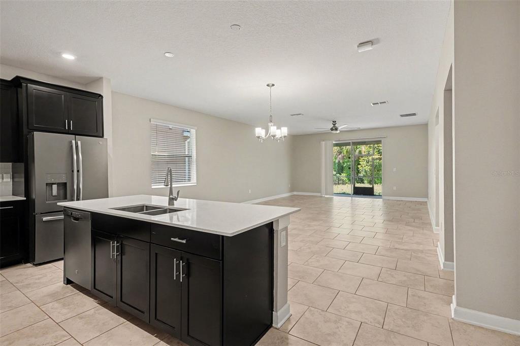 A kitchen with a dark island and stainless steel appliances opens to a living area — 467 BRUNSWICK DRIVE, DAVENPORT, FL
