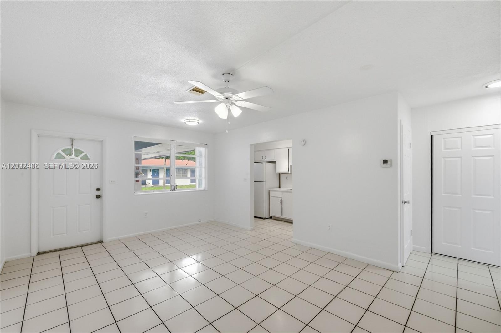 A bright, white-walled living area features tiled floors, a ceiling fan, and an adjacent kitchen — MIRAMAR, FL