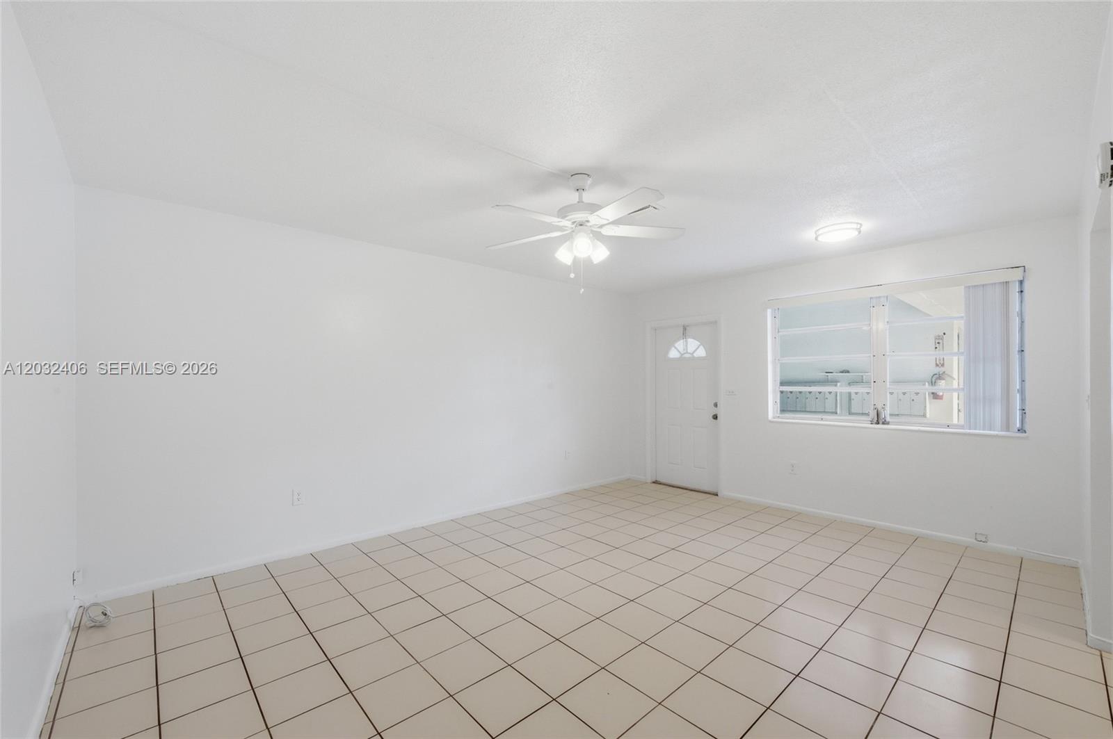 An empty room features white walls, beige tile flooring, a ceiling fan, and a window — MIRAMAR, FL