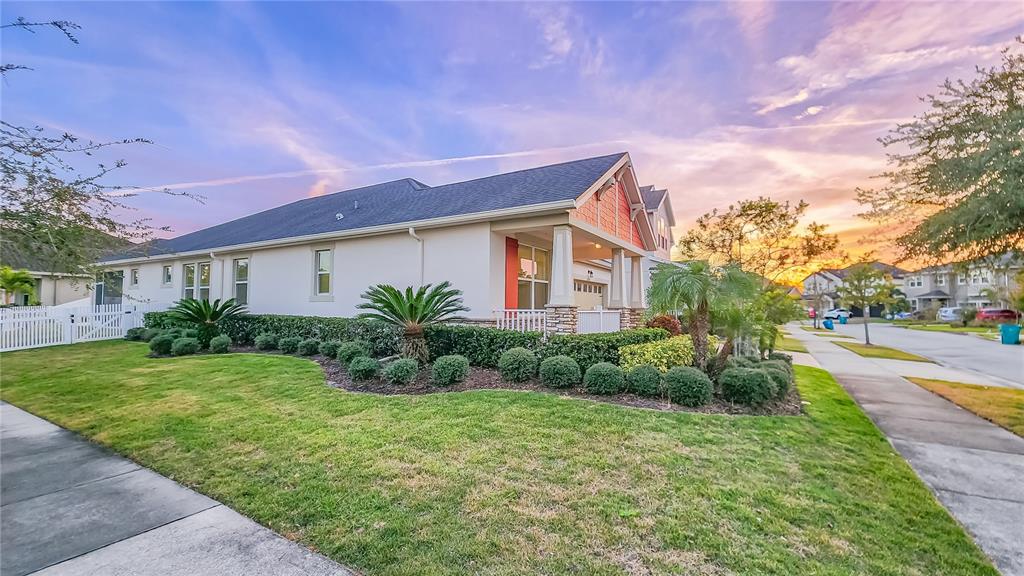 A side view of a suburban house with a lawn, landscaping, and a white fence — 8201 CORKFIELD AVENUE, ORLANDO, FL