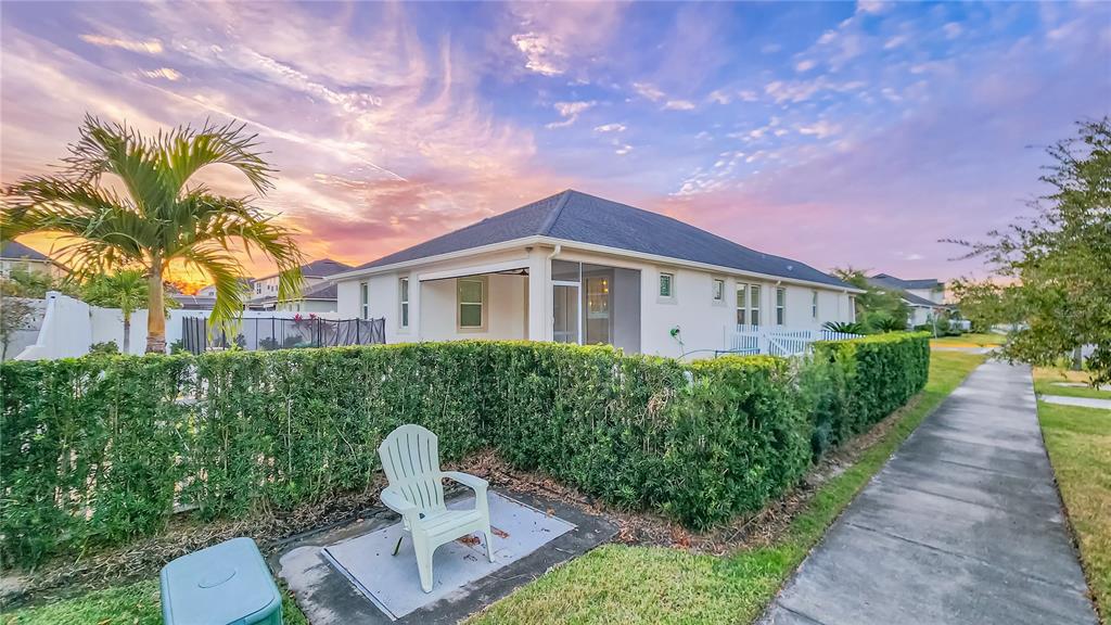 A white house with a screened-in patio sits behind a tall hedge at sunset — 8201 CORKFIELD AVENUE, ORLANDO, FL