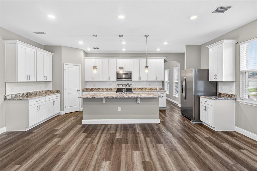 A kitchen features white cabinetry, granite countertops, a central island, and wood-look flooring — 801 PECAN AVENUE, SANFORD, FL