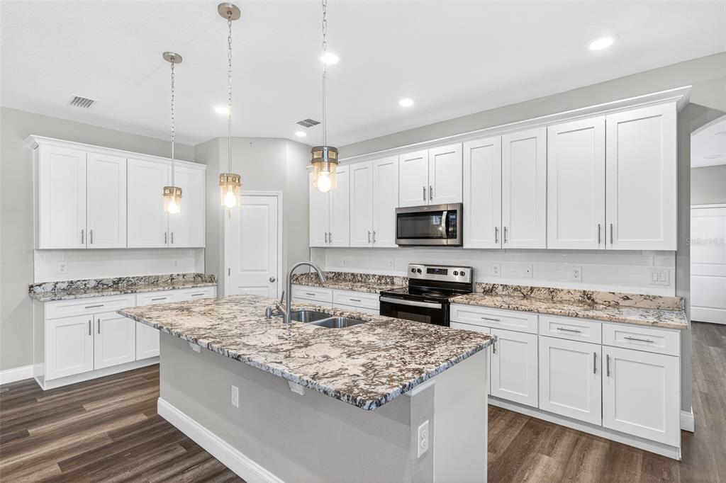 A kitchen features white cabinets, granite countertops, a central island, and stainless steel appliances — 801 PECAN AVENUE, SANFORD, FL