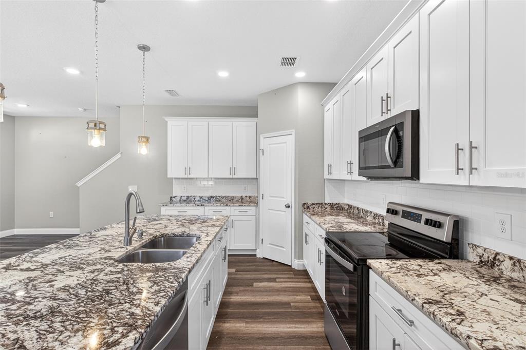 A modern kitchen features white cabinets, granite countertops, a large island, and stainless steel appliances — 801 PECAN AVENUE, SANFORD, FL
