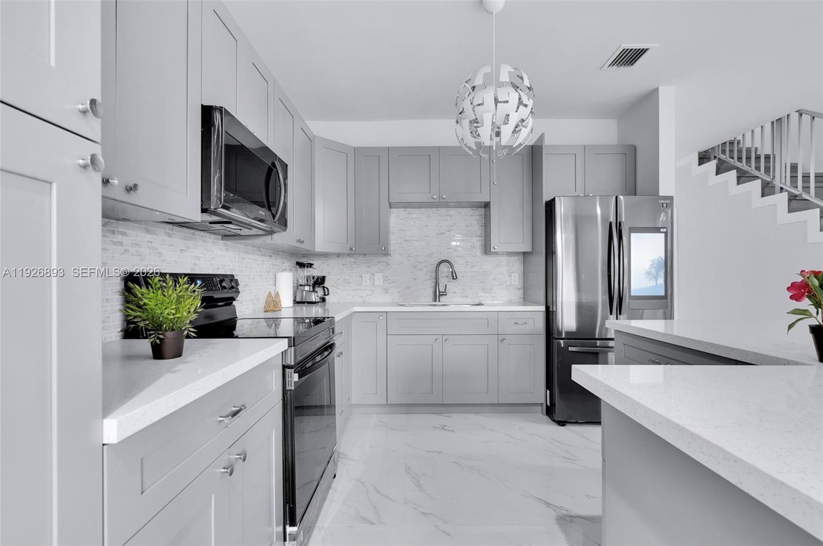 A modern kitchen features gray cabinets, stainless steel appliances, white countertops, and marble-look flooring — 1968 NW 25th Ave, Miami FL 33125, MIAMI, FL