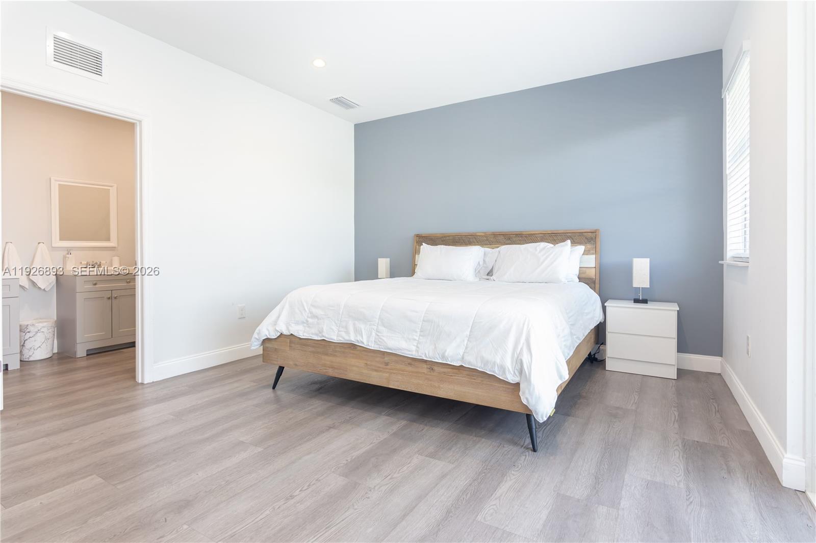 A bedroom features a wood-frame bed, a blue accent wall, and an attached bathroom — 1968 NW 25th Ave, Miami FL 33125, MIAMI, FL