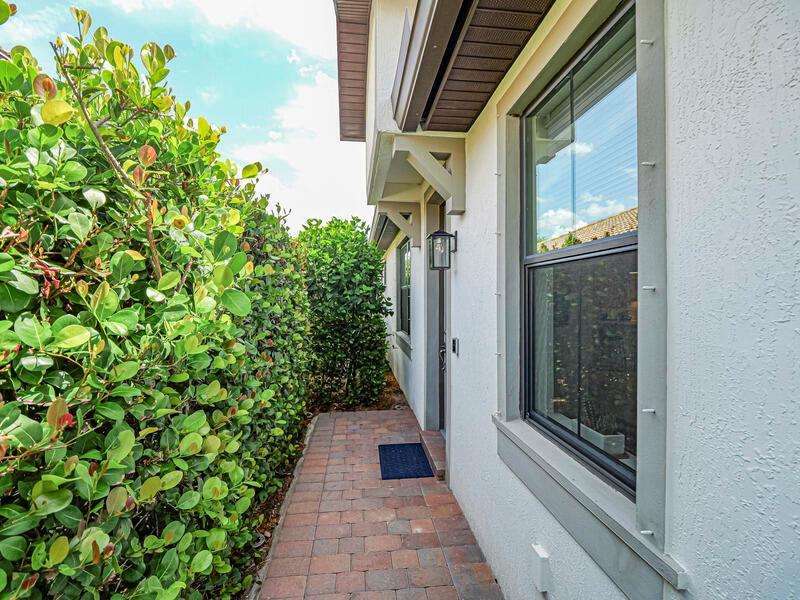 A paved walkway runs along the side of a house next to a large hedge — VERO BEACH, FL