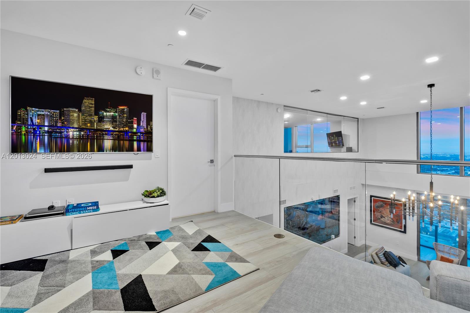 A modern loft living area features a wall-mounted television, glass railings, and light wood flooring — 121 NE 34th St, Miami FL 33137, MIAMI, FL