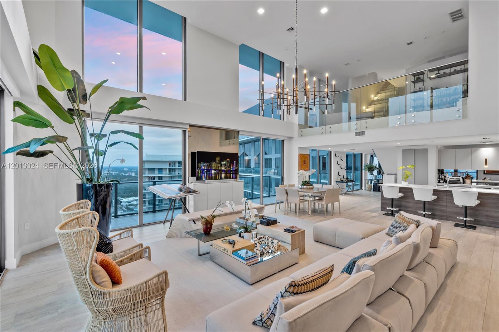 A modern, two-story living room features floor-to-ceiling windows, a large chandelier, and an open kitchen — 121 NE 34th St, Miami FL 33137, MIAMI, FL