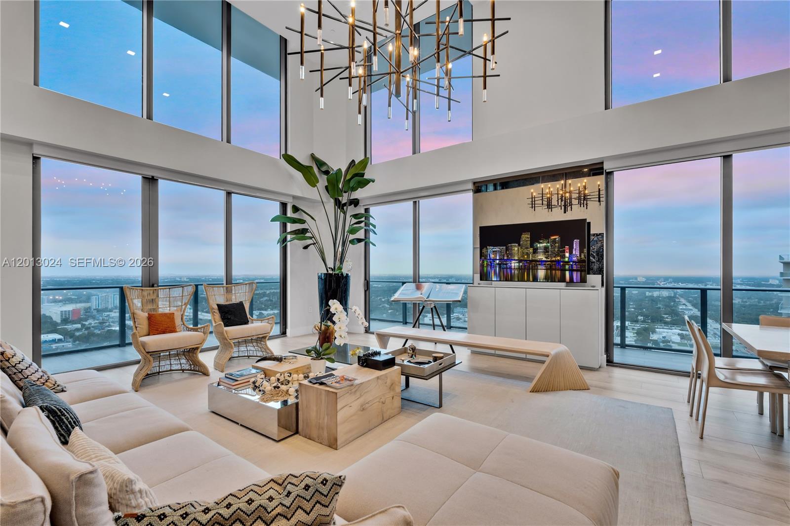 A modern, high-ceilinged living room features floor-to-ceiling windows, a large chandelier, and city views — 121 NE 34th St, Miami FL 33137, MIAMI, FL