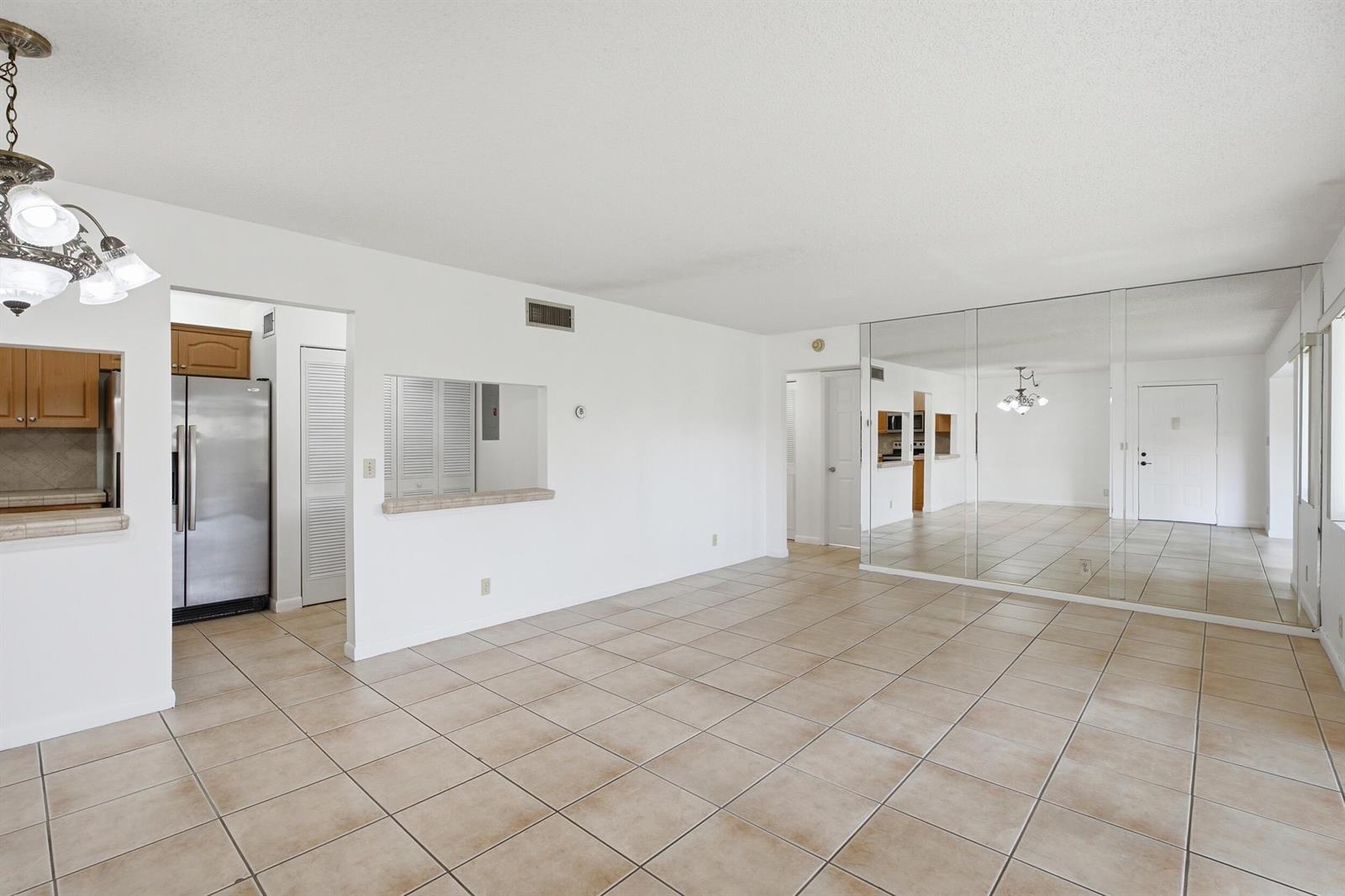 An open-concept living area features beige tile flooring, white walls, and a mirrored accent wall — 518 Shady Pine Way # B2, FL 33415, FL