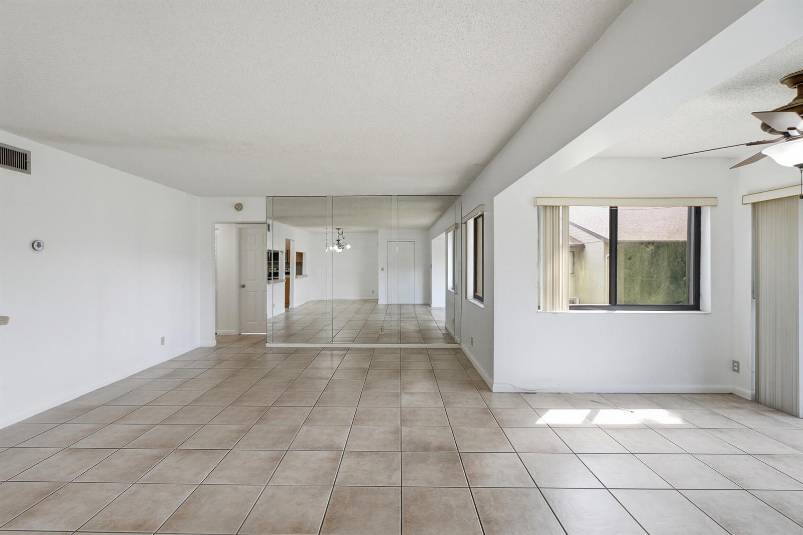 An empty room with beige tile flooring, white walls, a mirrored wall, and a ceiling fan — 518 Shady Pine Way # B2, FL 33415, FL