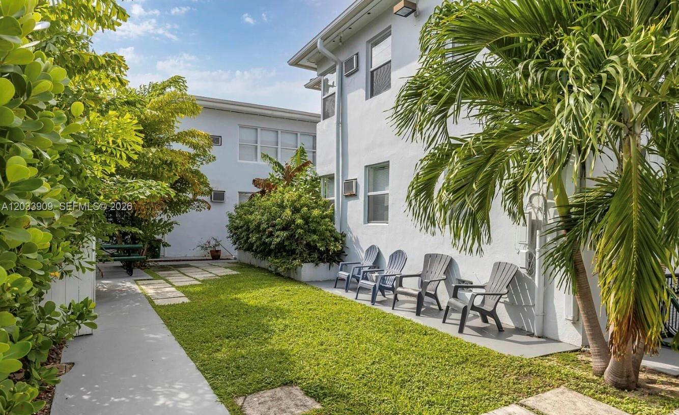 A grassy courtyard with a paved walkway, palm trees, and a row of outdoor chairs — 9473 Abbott Ave # 5, Surfside FL 33154, SURFSIDE, FL