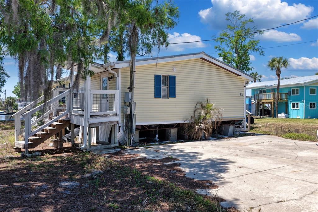 A yellow mobile home with blue shutters and a wooden deck sits on a lot — 53 SE 241ST STREET, SUWANNEE, FL