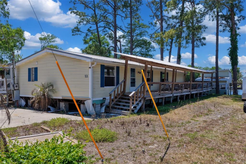 A yellow mobile home with a long wooden porch and stairs sits on a lot — 53 SE 241ST STREET, SUWANNEE, FL