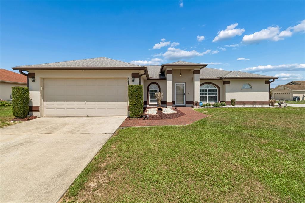 A single-story house with a beige stucco exterior, a two-car garage, and a brick walkway — 6352 PROMINENCE POINT DRIVE, LAKELAND, FL