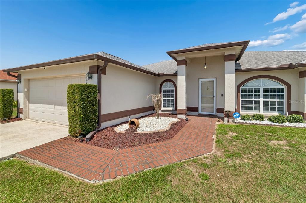 A single-story house exterior features a brick walkway, a garage, and a covered front entrance — 6352 PROMINENCE POINT DRIVE, LAKELAND, FL