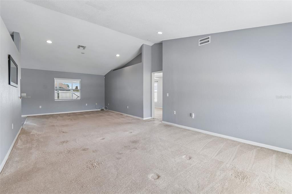 An empty living room features gray walls, a vaulted ceiling, and beige wall-to-wall carpeting — 6352 PROMINENCE POINT DRIVE, LAKELAND, FL