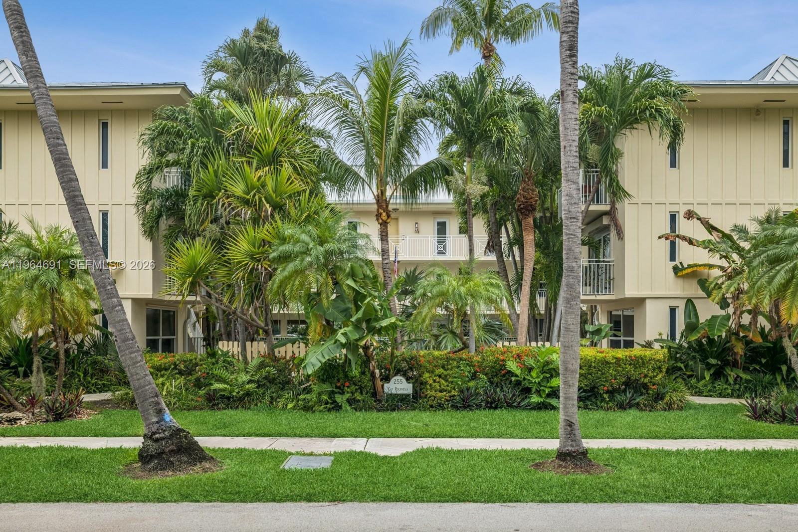 A three-story apartment building with light-colored siding is surrounded by lush tropical landscaping and palms — 255 Sunrise Dr # 107, Key Biscayne FL 33149, KEY BISCAYNE, FL