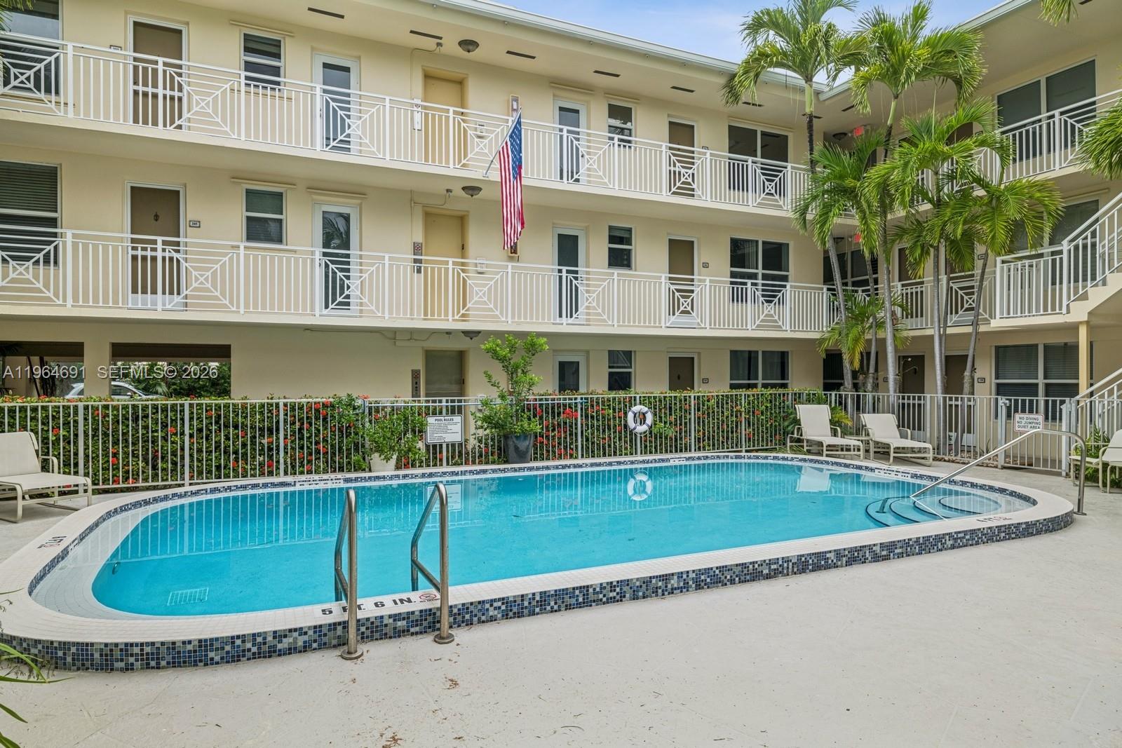A swimming pool sits in the courtyard of a multi-story apartment building with balconies — 255 Sunrise Dr # 107, Key Biscayne FL 33149, KEY BISCAYNE, FL