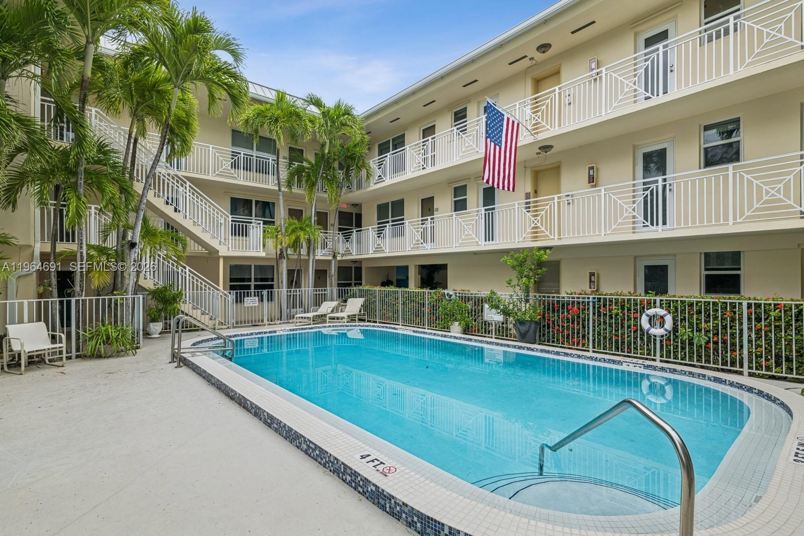 A swimming pool sits in the courtyard of a multi-story apartment building with balconies — 255 Sunrise Dr # 107, Key Biscayne FL 33149, KEY BISCAYNE, FL