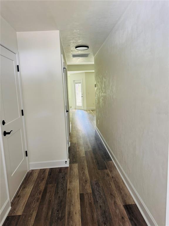 A hallway with wood-look flooring leads toward a doorway with natural light — 8030 NE 102ND COURT, BRONSON, FL