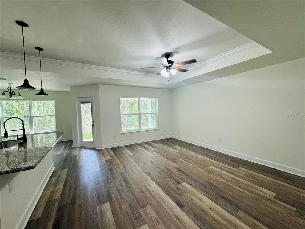 An open-concept living area features wood-look flooring, a tray ceiling, and a kitchen island — 8030 NE 102ND COURT, BRONSON, FL