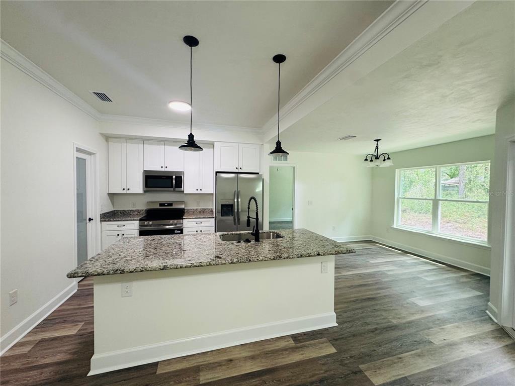 A kitchen with white cabinets, granite countertops, and an island opens to a dining area — 8030 NE 102ND COURT, BRONSON, FL