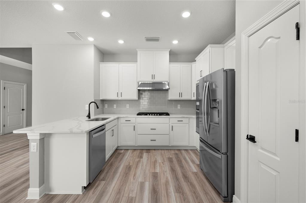 A modern kitchen features white cabinets, stainless steel appliances, and a marble-patterned island countertop — 7665 SOMERSWORTH DRIVE, KISSIMMEE, FL