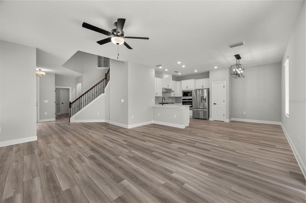 An open-concept living area with light wood-look flooring, a ceiling fan, and a modern kitchen — 7665 SOMERSWORTH DRIVE, KISSIMMEE, FL