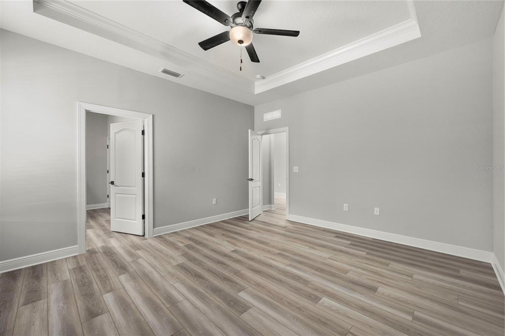 An empty bedroom features light gray walls, wood-look flooring, and a tray ceiling with a fan — 7665 SOMERSWORTH DRIVE, KISSIMMEE, FL