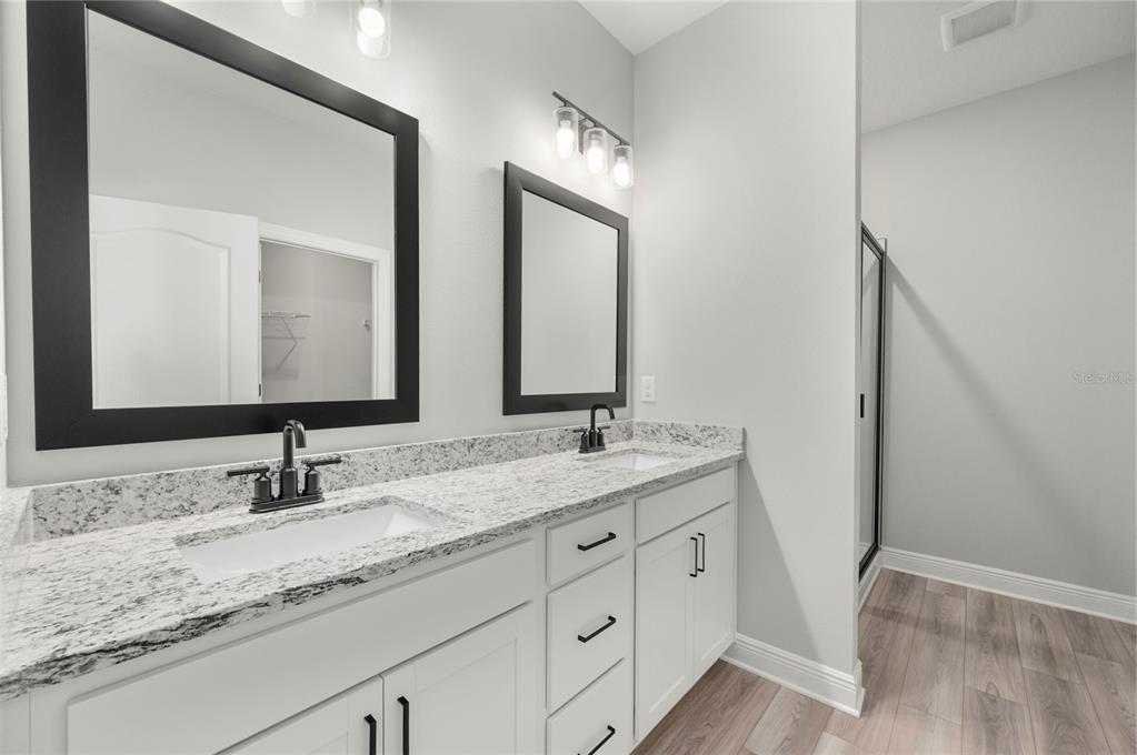 A bathroom with a double vanity, white cabinets, granite countertops, and two black-framed mirrors — 7665 SOMERSWORTH DRIVE, KISSIMMEE, FL