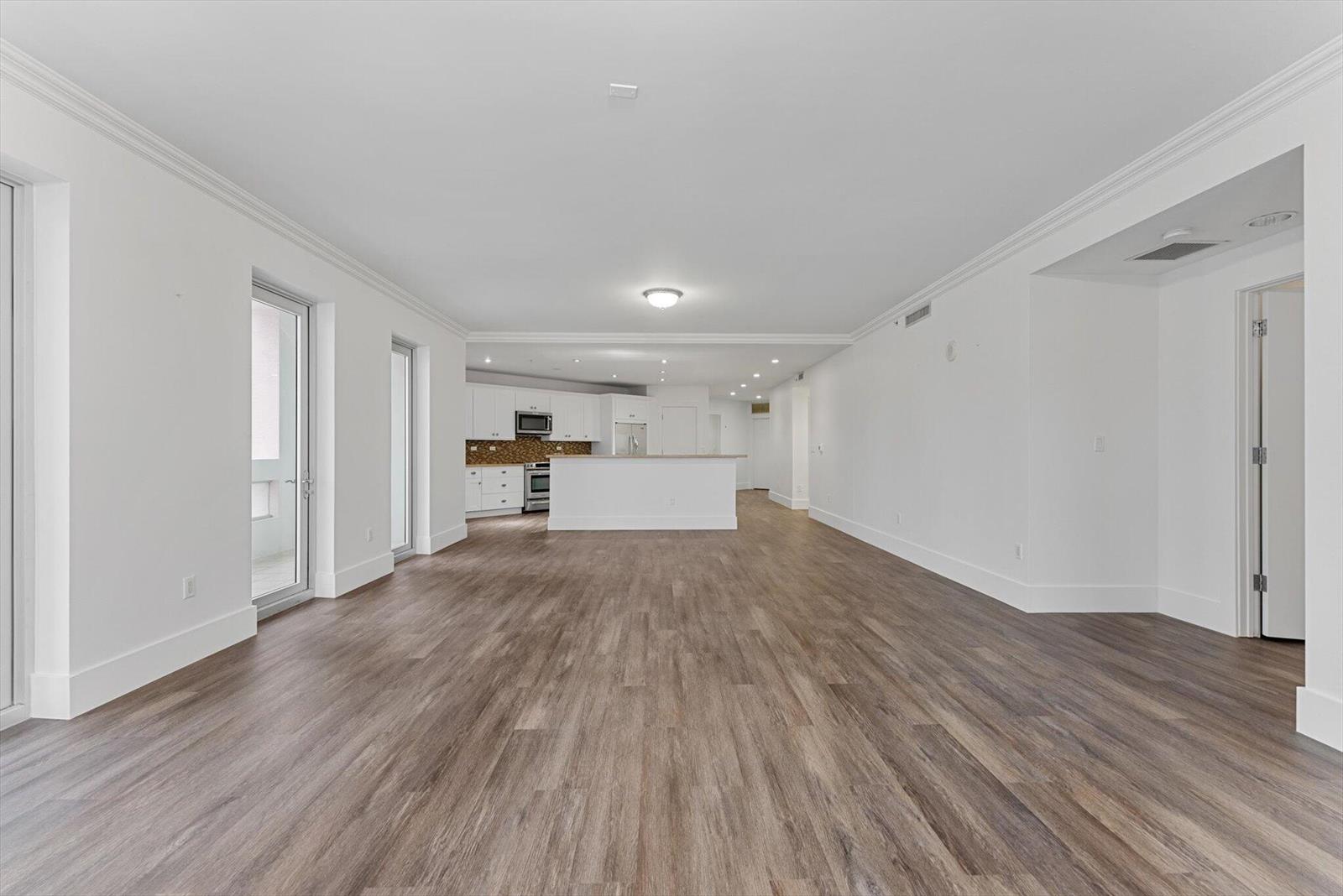 An open-concept living area features wood-look flooring, white walls, and a kitchen with white cabinetry — 455 E Palmetto Park Road # 6e, Boca Raton FL 33432, BOCA RATON, FL