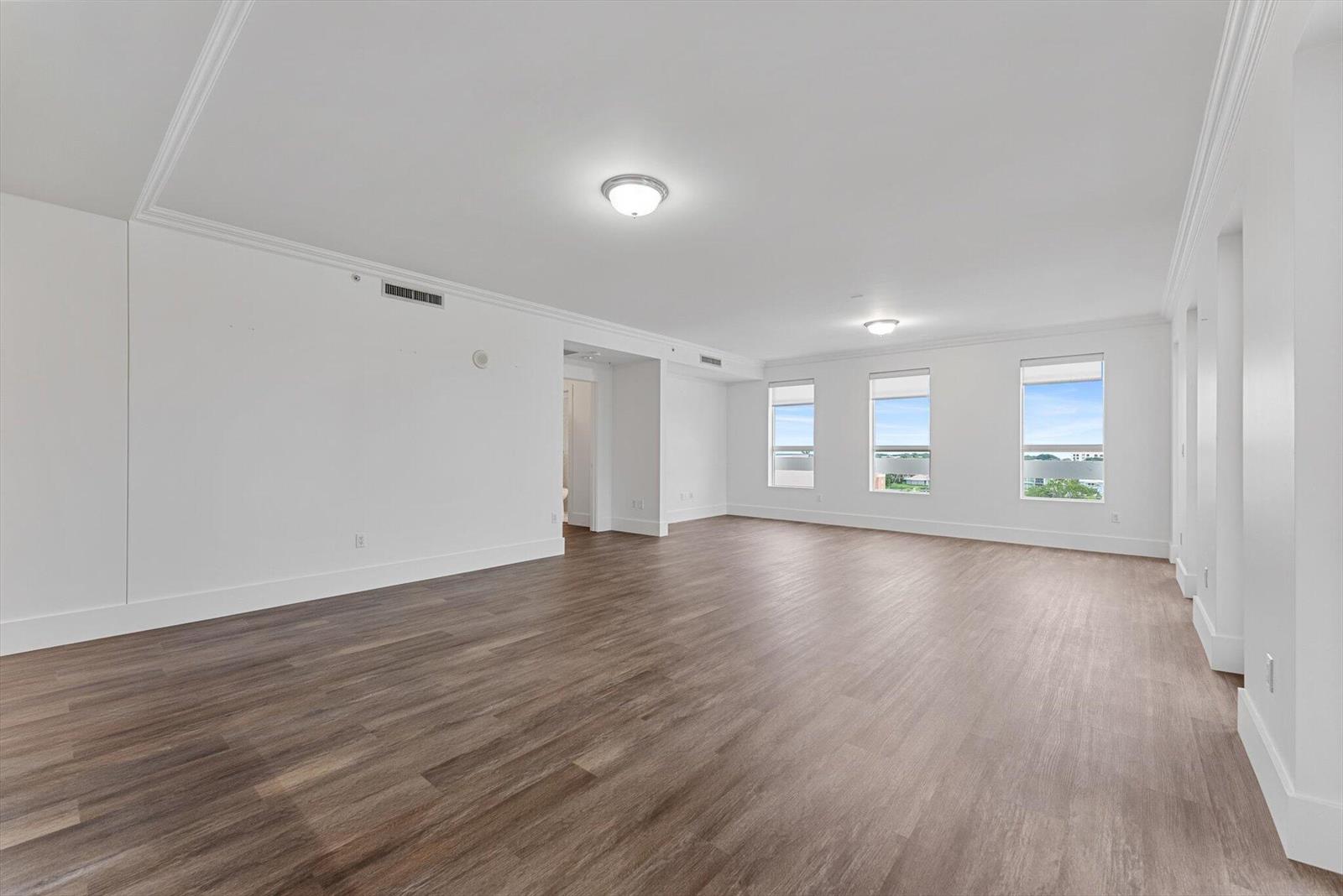 An empty room features white walls, wood-look flooring, crown molding, and three windows — 455 E Palmetto Park Road # 6e, Boca Raton FL 33432, BOCA RATON, FL