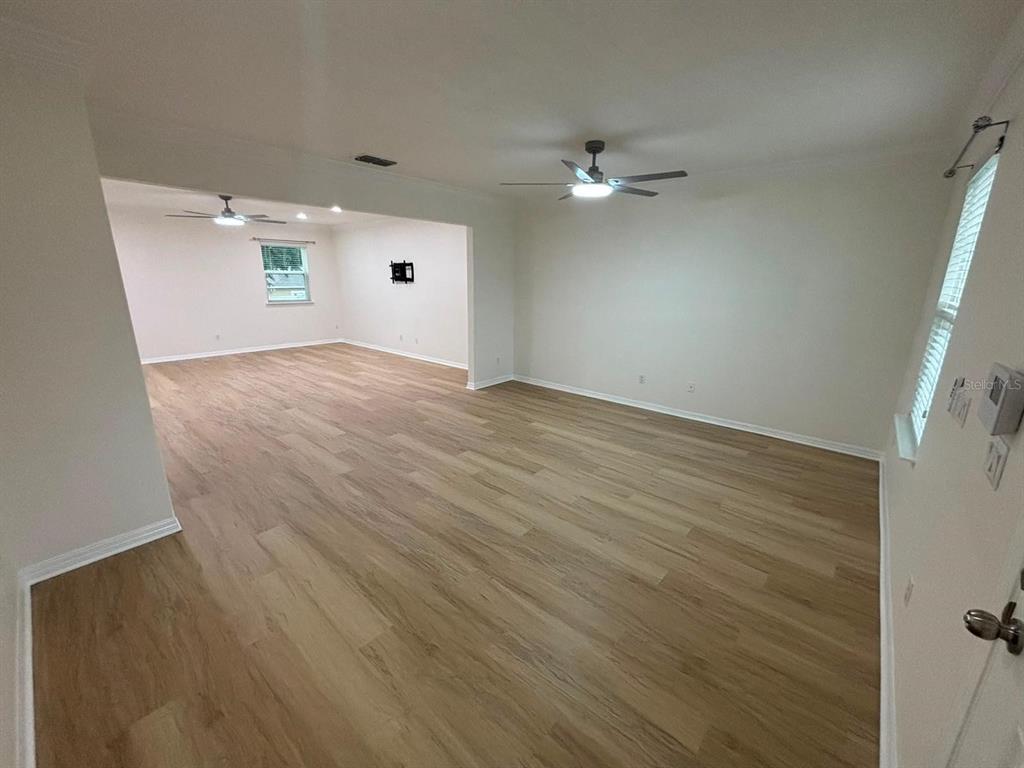 An empty living area with light wood-look flooring, white walls, and two ceiling fans — 1236 WATER WILLOW DRIVE, GROVELAND, FL