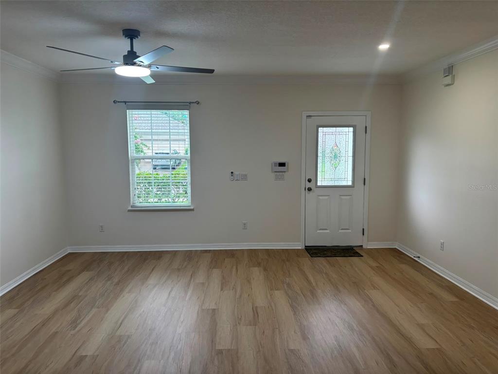 An empty room features light wood-look flooring, a ceiling fan, a window, and an entry door — 1236 WATER WILLOW DRIVE, GROVELAND, FL