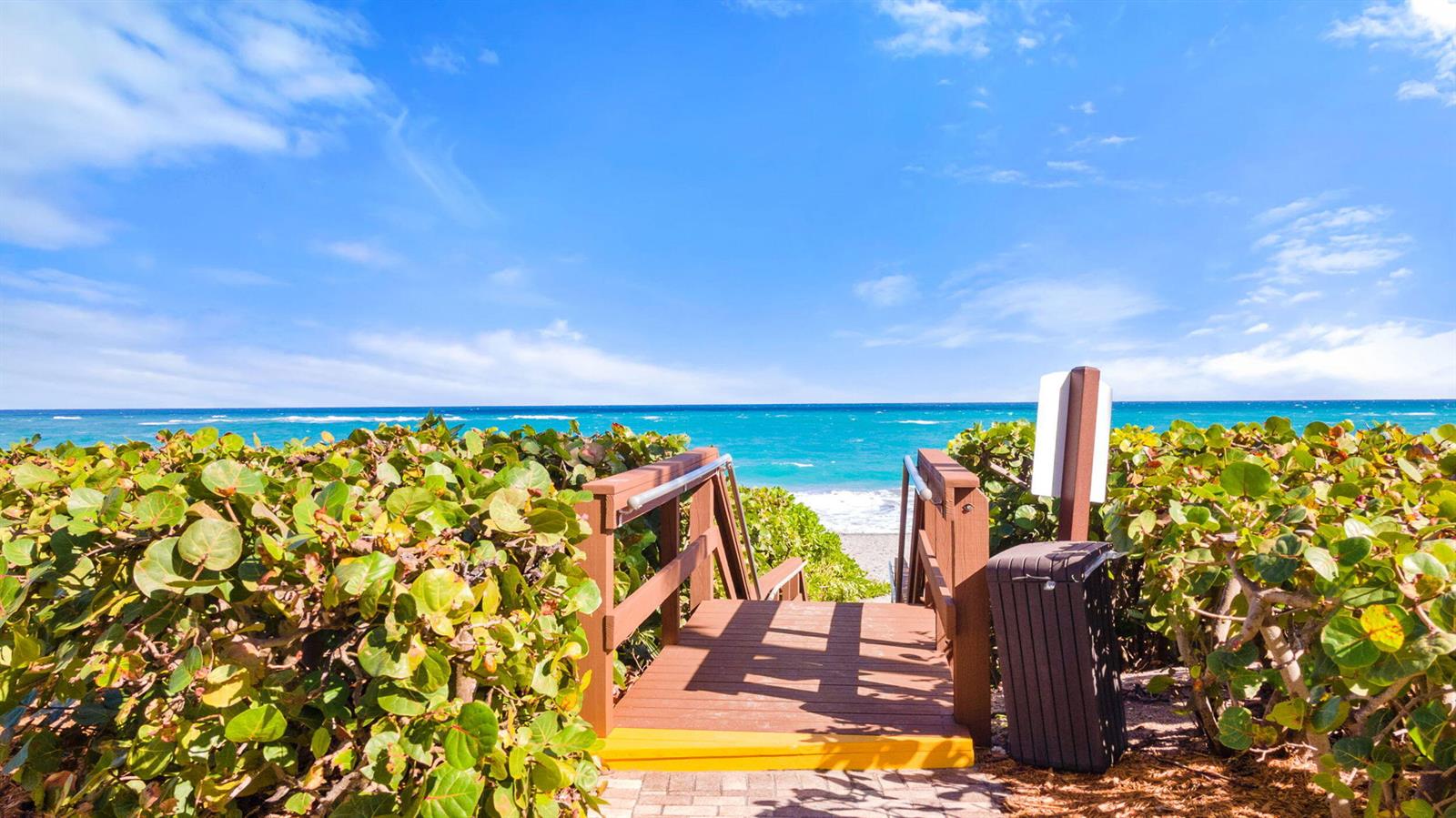 A wooden staircase leads through lush green bushes toward a sunny beach and ocean — 400 Ocean Trail Way # 205, Jupiter FL 33477, JUPITER, FL