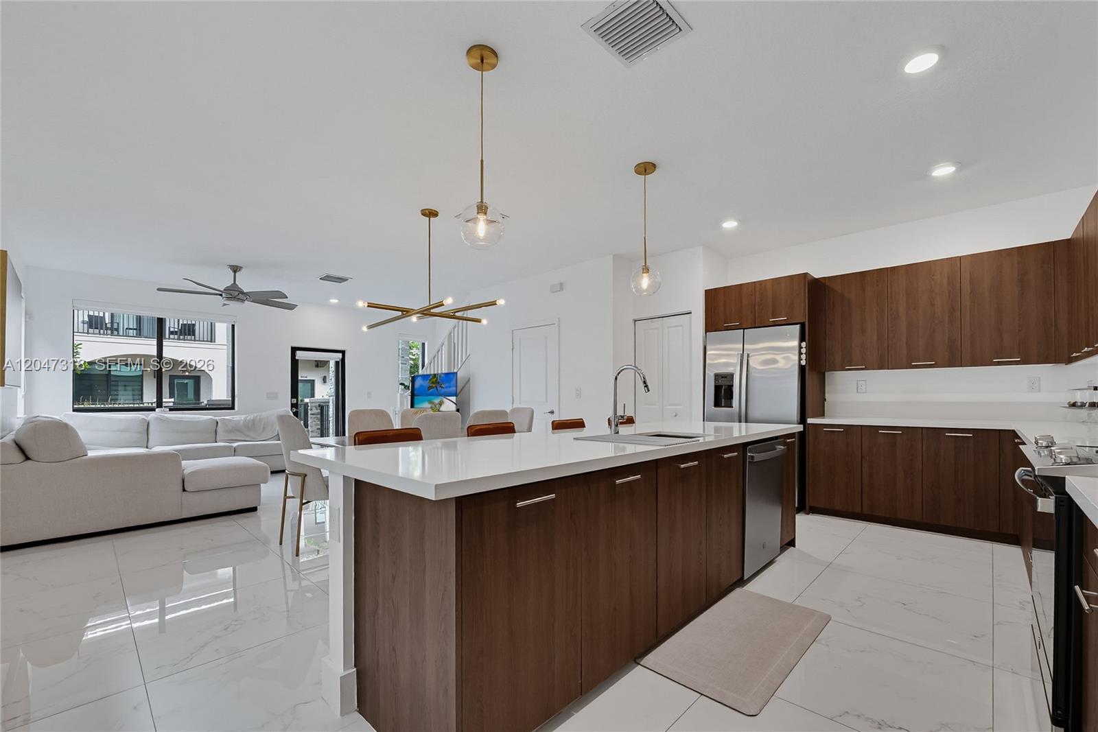 A modern kitchen with wood cabinets and a white island opens into a living area — 4605 NW 83rd Path, Doral FL 33166, DORAL, FL