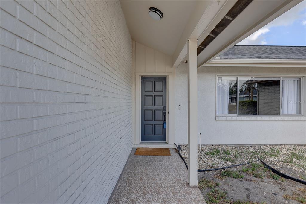 A covered entryway features a dark blue front door, white brick walls, and a window — 3718 PENRICK DRIVE, HOLIDAY, FL